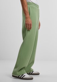 Groene joggingbroek met een ontspannen pasvorm, textuurstof en zijzakken. Accentueren met zichtbare stiksels en gedragen met witte sneakers.