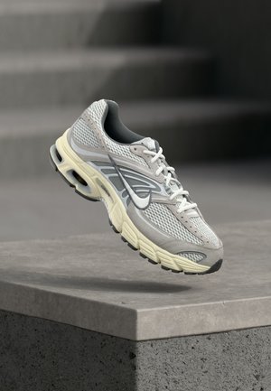 Grauer und weißer Nike-Laufschuh mit gepolsterter Sohle, der über einer Betontreppe im Freien schwebt.
