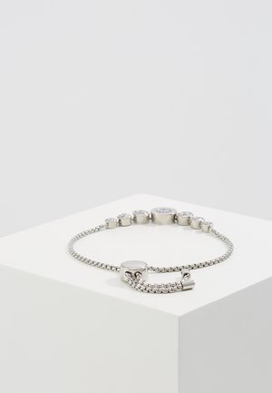 Adjustable silver chain bracelet with round clear gemstones set in varying sizes along the top, resting on a white pedestal.