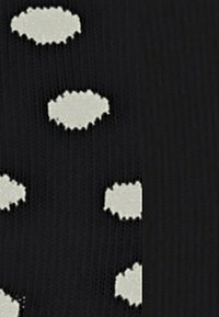 Der schwarze Strickstoff weist unregelmäßig geformte, gewellte weiße Pünktchen auf. Die Textur erscheint glatt mit einem leichten Stretch.