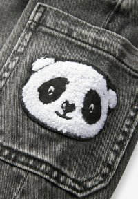 Patch avec visage de panda texturé blanc et noir cousu sur une poche en jean gris avec des coutures visibles.