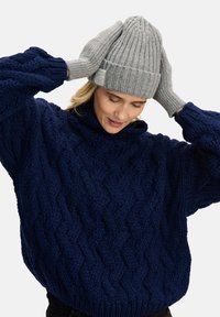 Granatowy, oversize'owy sweter z dzianiny z wypukłym wzorem warkocza, zestawiony z szarą, prążkowaną czapką i pasującymi rękawiczkami.