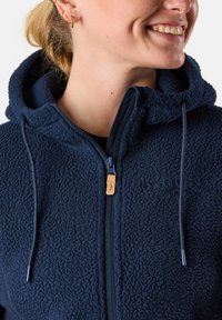 Navy fleece hoodie with textured surface, front zipper, and adjustable drawstrings. Features embroidered logo and faux leather zipper pull.