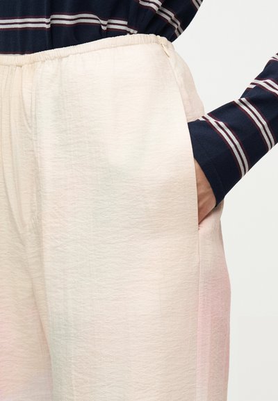 Χέρι στην τσέπη χαλαρών, ανοιχτό ροζ παντελονιών με ελαστική μέση, σε συνδυασμό με μπλε σκούρο μπλουζάκι μακρυμάνικο με λευκές και κόκκινες ρίγες.