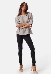 Blusa grigia chiaro, texture con maniche a sbuffo, abbinata a pantaloni skinny neri e tacchi color nudo. La blusa ha una silhoutte a peplo.