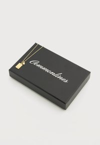 Μαύρο ορθογώνιο κουτί με το κείμενο «Commonlines» σε λευκό και λεπτή χρυσή αλυσίδα με ορθογώνιο μενταγιόν και μικρό στρογγυλό κόσμημα στην κορυφή.