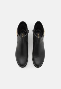 Bottes noires en cuir jusqu'à la cheville avec une finition texturée, fermeture éclair latérale et accents en matériel doré. Design à bout rond et semelle plate.