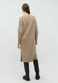 Beige ribstrikket lang kjole med side slids. Har lange ærmer og rund halsudskæring, parret med knæhøje sorte støvler.