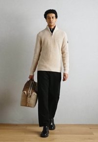 Suéter de canalé crema con cuello alto, pantalones de pierna ancha negros y zapatos negros. Lleva un bolso de color claro con cremallera.