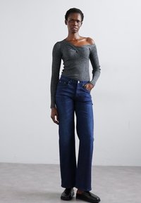 Jeans anchos de color azul oscuro combinados con una camiseta ajustada de manga larga gris con un diseño fuera del hombro. Texturas suaves y estilo casual.