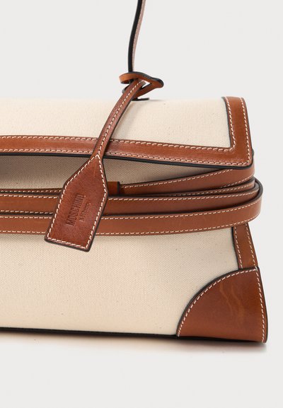 Μπεζ καμβά τσάντα χειρός με καφέ δερμάτινες λεπτομέρειες, λευκό ράψιμο, δερμάτινο λουρί με θηλιά και δερμάτινη ετικέτα με ανάγλυφο το όνομα της μάρκας.