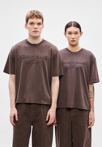 Brune bomuld t-shirts med korte ærmer, der har præget "TOMMY JEANS" tekst. Løs pasform, kombineret med matchende brune bukser.