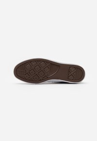 Biała podeszwa sneakerów z brązowym gumowym spodem, z wzorem diamentowej trawy i wytłoczonym logo na pięcie.