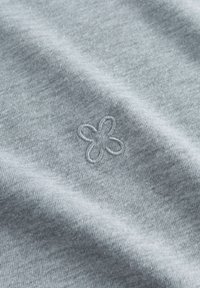 Hellgrauer Baumwollstoff mit weicher Textur, verziert mit einer kleinen, gestickten Blume in einem etwas dunkleren Grau.
