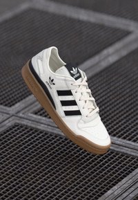 Bijele kožne tenisice s crnim trostrukim prugama, gumeni đon u boji gume i podstavljeni ovratnik s Adidas logom na jeziku.