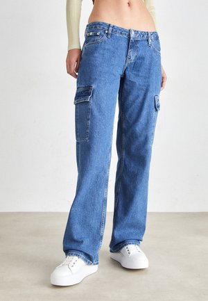 Pantaloni cargo in denim blu con una vestibilità rilassata, dotati di tasche laterali, chiusura a bottone e lievi sbiadimenti, abbinati a sneaker bianche.