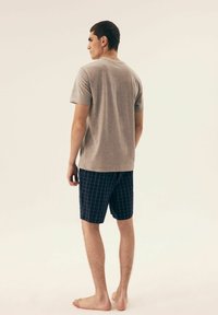 Szara, krótka koszulka z miękkiego materiału. Niebieskie szorty w kratkę o wygodnym kroju. Model stoi boso, tyłem.