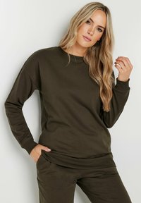 Sudadera verde oliva de tejido suave con cuello redondo, mangas largas y puños acanalados, que presenta un corte holgado y sin patrones visibles.