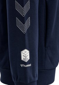Felpa navy con strisce orizzontali e grafiche a chevron bianche. Presenta una stampa del logo sulla manica, realizzata in tessuto morbido.