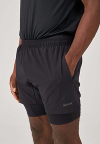 Black athletic shorts made from lightweight fabric, featuring an elastic waistband, side pockets, and a fitted inner short layer.