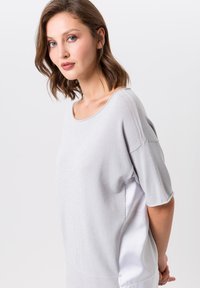 Haut à manches courtes gris clair avec un devant en tricot texturé, des côtés en satin et une coupe ample avec un décolleté large.
