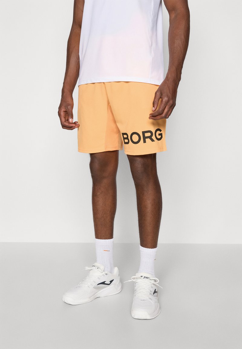 Orange shorts with black "BORG" text on the side, made of lightweight fabric. Paired with a white shirt and white sneakers.