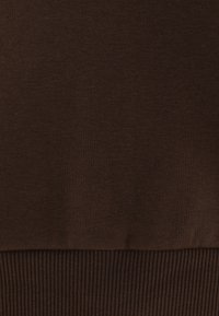 Sudadera marrón con una textura suave y lisa, con acentos de canalé en el dobladillo. La tela parece ligera y elástica.