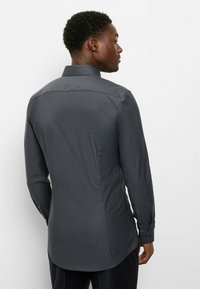 Dunkelgraues Hemd mit geometrischem Muster, langen Ärmeln, Manschetten mit Knöpfen und spitzem Kragen. Glatte Textur und taillierte Passform.