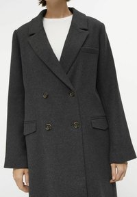 Abrigo de mezcla de lana en gris oscuro con un diseño de doble botonadura, solapas con muescas, dos bolsillos frontales y botones de bronce. Tejido texturizado.