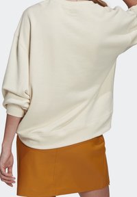 Krämfärgad oversized sweatshirt med rund hals, ribbade manschetter och subtil branding på baksidan. Kombinerad med en senapsgul minikjol.