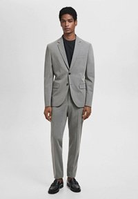 Blazer grigio e pantaloni abbinati in una vestibilità slim, realizzati in tessuto liscio. Gli accenti includono una chiusura con un bottone e tasche. Scarpe nere.