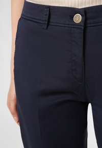 Marineblaue Hose mit glatter Textur, Reißverschluss und Knopfverschluss. Verfügt über Gürtelschlaufen und seitliche Taschen. Geeignet für Freizeitkleidung.