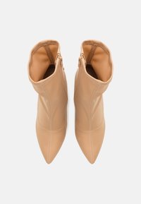 Botas de tobillo beige con punta afilada y material de cuero suave, que cuentan con cremalleras expuestas en cada lado exterior y una textura lisa.