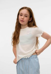 Krämfärgad kortärmad t-shirt med volangärmar och en liten, broderad cirkulär design på bröstet. Har en avslappnad passform.