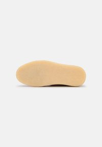 Suela de un zapato, hecha de goma de un beige claro, textura lisa, con forma redondeada, presentando una superficie limpia y plana sin patrones.