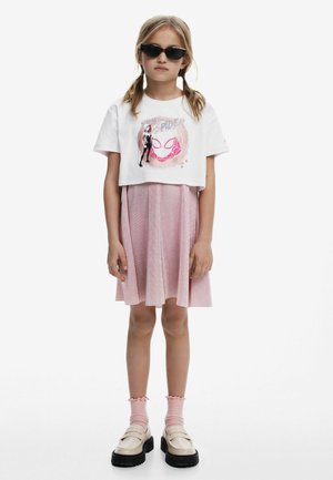 Vit kortärmad T-shirt med grafik, rosa glittrig kjol, ribbade rosa strumpor och krämfärgade platåskor; eleganta svarta solglasögon fulländar outfiten.