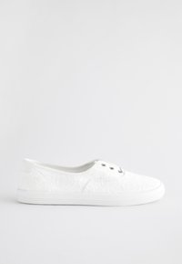 Baskets en dentelle blanche avec un motif floral texturé, deux œillets et une semelle en caoutchouc blanche. Le design est bas avec un bout arrondi.