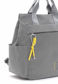 Sac à dos en tissu texturé gris avec une poche zippée à l'avant, une poche latérale, des poignées grises et un porte-clés en cuir jaune attaché à un mousqueton argenté.