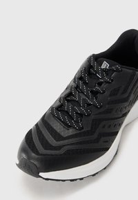 Black and white athletic shoe with patterned laces, mesh and synthetic upper, and a thick white sole on a plain background.