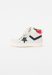 Vit hög sneakers av läder, med en marinblå stjärna och chevronmönster, röd hälaccent och beige snören. Texturerad tåhuvud.