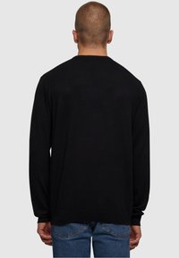 Schwarzer langer Pullover mit rundem Ausschnitt, aus weichem Stoff. Hat einen entspannten Schnitt sowie gerippte Bündchen und Saum.