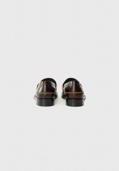 Bruine leren schoenen met een gladde afwerking, open achterkant en minimale stikseldetails. Licht verhoogde hak. Donkere, geprofileerde zool.