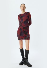 Langsleeve jurk in een rode en paarse tie-dye patroon, met zijruche. Gepaard met kniehoge zwart leren laarzen met stevige zolen.
