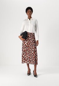 Camicia bianca a maniche lunghe, gonna midi a stampa leopardata con spacco, borsa nera strutturata e scarpe con tacchi alti nere. Materiali lisci e strutturati.