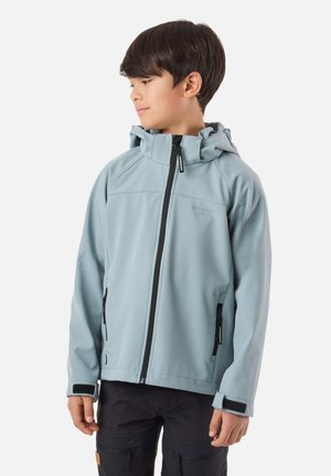 Chlapec oblečený v svetlomodrej kapucňovej bunde na zips s čiernymi detailmi na zipsoch a tmavých nohaviciach, pozerajúci sa doľava na bielom pozadí.