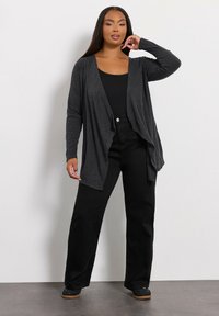 Svart lättviktscardigan med draperad design, som har en texturerad grå tyg, öppen fram och långa ärmar, kombinerad med svarta byxor.