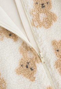 Giacca in pile color crema con motivo orsetto, dotata di zip color crema e tessuto morbido. Notevole per il suo materiale soffice e l'aspetto caldo.