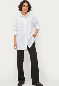 Witte oversized overhemd met kraag, lange mouwen opgerold, gecombineerd met zwarte wijde broek en zwarte schoenen.