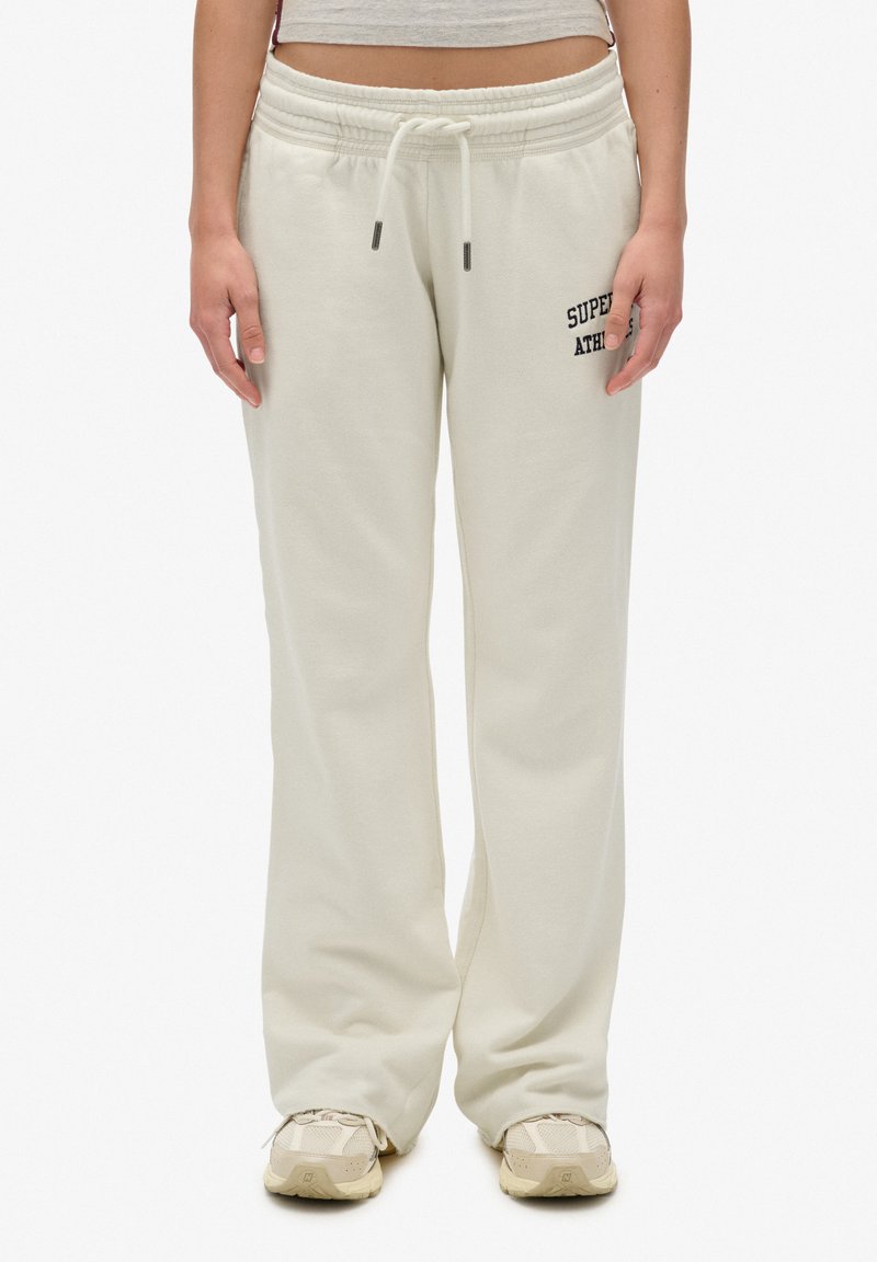 Crème-kleurige joggingbroek van zacht materiaal, met een trekkoord in de taille, een relaxte pasvorm en "SUPER ATLEET" geborduurd op de dij.