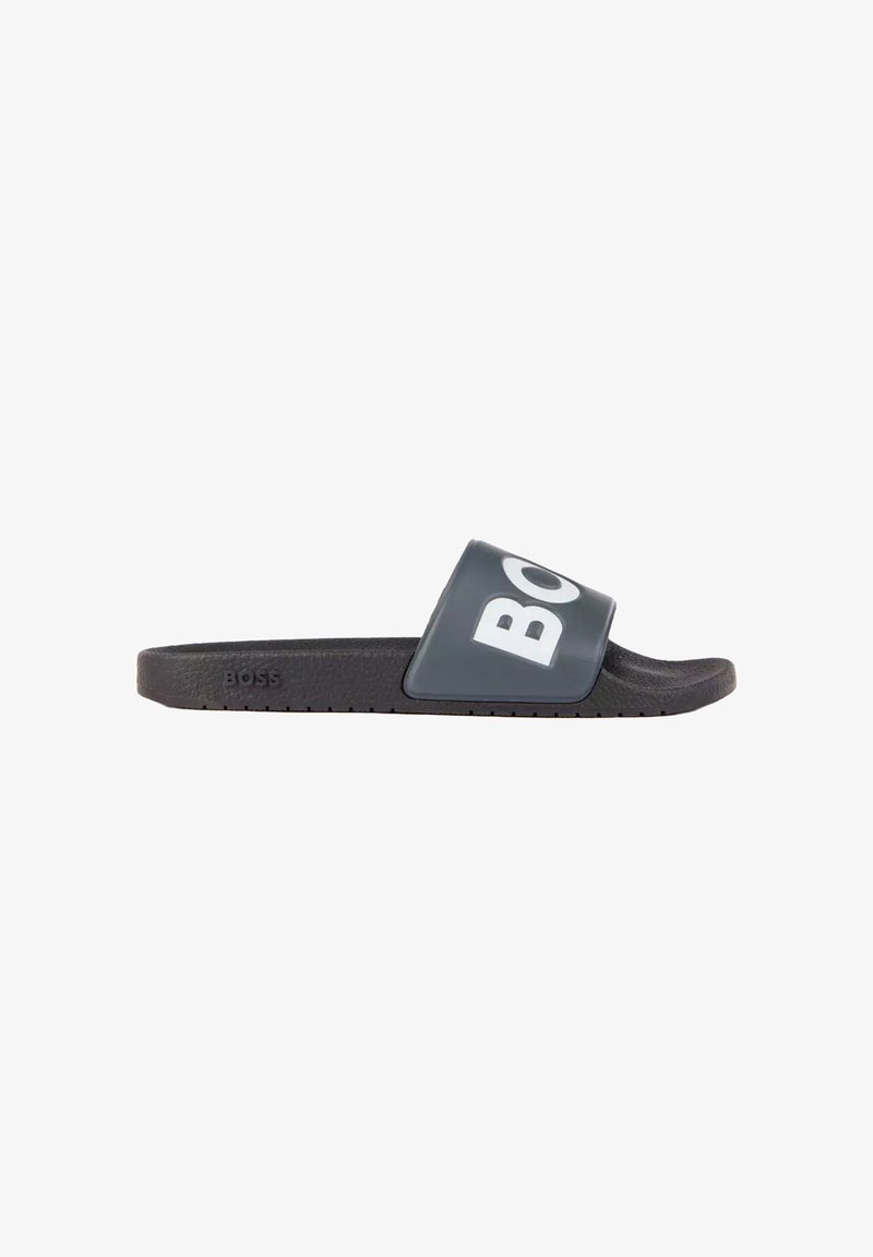 Sandale slide noire avec une large bride portant un grand texte blanc "BOSS", semelle texturée et logo "BOSS" embossé sur le côté.